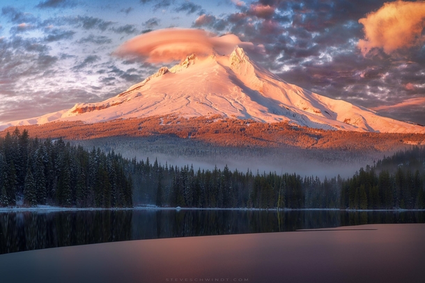 A freshly snowed Mt Hood holds on to the final moments of sunlight as fog rolls in at Trillium Lake Oregon 
