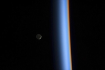 A crescent moon rises over the cusp of the Earths atmosphere