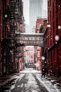 A snowy lonely daytime NYC Street completed by a catwalk overhead and skyscrapers in the background