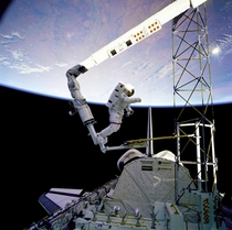 Astronaut Jerry L Ross anchored to the foot restraint on the RMS approaches the tower-like ACCESS device The structure was just deployed by Ross and astronaut Sherwood Spring as the Atlantis flies over white clouds and blue ocean waters of the Atlantic De