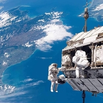 Astronauts working outside the International Space Station ISS in  New Zealand behind them