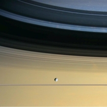 Cassini captured Saturns icy moon Dione floating in front of Saturn amp the rings which are seen nearly edge on casting shadows on the cloud tops