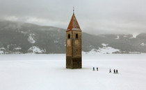 Church steeple peeking out of a frozen lake in the village of Graun 