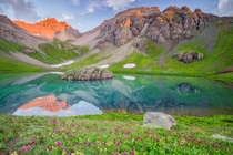 Early morning light over a field of wildflowers and crystal blue lake in the San Juan Mountains Colorado  by Jason Hatfield