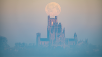 Full Snow Moon setting over Ely Cathedral that dates back to  in Romanesque style featuring a central octagonal tower