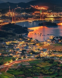 Massive industrial port seen across the bay from a sleepy fishing village in Yeosu South Jeolla Province South Korea 
