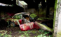 Moss-covered car in garage of abandoned house in British countryside 