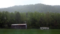 Rain falls on a beautiful abandoned barn and trailer out in a field in Cosby TN 