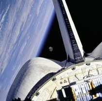 The moon is framed between the Space Shuttle orbiters OMS Orbital Maneuvering System pod and the Earth limb over the Atlantic Ocean as seen from the aft windows onboard Discovery on mission STS- 