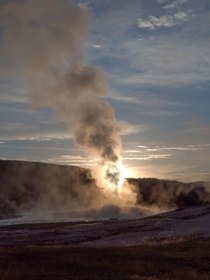 The sun rising from behind the steam of Old Faithful Yellowstone 