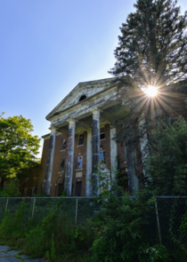 The sun shines through the trees at an abandoned psychiatric hospital in New England 